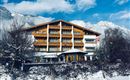 A cozy hotel in the mountains with several floors. The surroundings are snow-covered and the mountains are visible in the background.