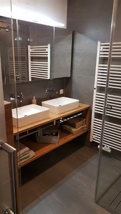 A modern bathroom with two sinks and wooden shelves. The space is elegant and well-structured with modern fixtures.