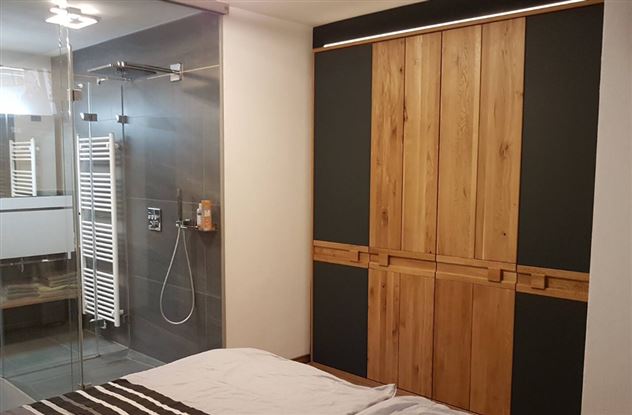 A modern bedroom with a wooden wardrobe and a glass shower. The walls are painted in neutral tones, creating a cozy atmosphere.