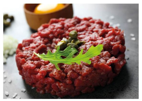 A fresh beef tartare on a black background, garnished with capers and a leaf of arugula. In the background, a yolk in a bowl is visible.