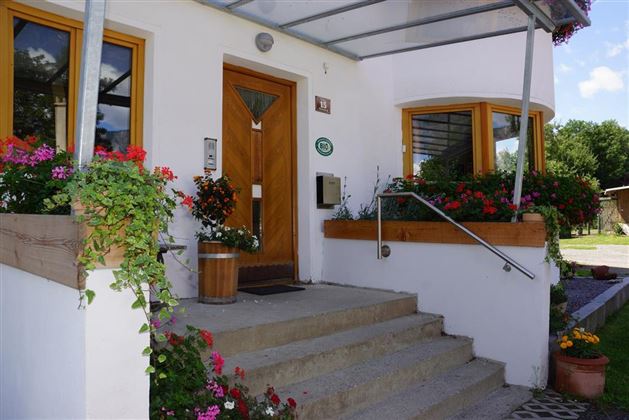 Ein einladender Hauseingang mit blühenden Pflanzen und einer schönen Treppe. Die große Veranda bietet Schutz und Licht.