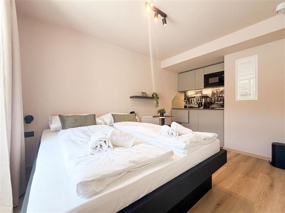 Ein modernes Schlafzimmer mit zwei Betten und frischen Handtüchern. Im Hintergrund ist eine offene Küchenzeile sichtbar.