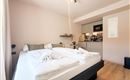 Ein modernes Schlafzimmer mit zwei Betten und frischen Handtüchern. Im Hintergrund ist eine offene Küchenzeile sichtbar.