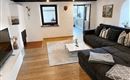 Ein gemütliches Wohnzimmer mit einem großen, grauen Sofa und einem flachen Fernseher. Der Raum hat Holzbalken an der Decke und einen warmen Holzboden.