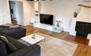 Ein modernes Wohnzimmer mit einer großen Couch und einem Fernseher. Der Raum hat Holzdeckenbalken und einen Kamin, der für Gemütlichkeit sorgt.