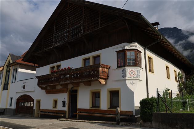 Ein traditionelles Haus mit einem großen Balkon und kunstvollen Verzierungen. Die Fassade ist weiß und die Umgebung ist malerisch.
