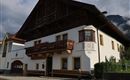 Ein traditionelles Haus mit einem großen Balkon und kunstvollen Verzierungen. Die Fassade ist weiß und die Umgebung ist malerisch.