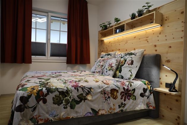 Ein gemütliches Schlafzimmer mit einem großen Bett und bunten Blumenbettwäsche. Die Wände sind aus Holz, und das Zimmer hat große Fenster mit roten Vorhängen.