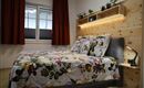 Ein gemütliches Schlafzimmer mit einem großen Bett und bunten Blumenbettwäsche. Die Wände sind aus Holz, und das Zimmer hat große Fenster mit roten Vorhängen.