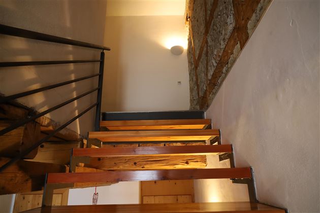 Eine Treppe aus Holz mit einer modernen Geländer. An der Wand ist ein Steinmuster zu sehen, und im Hintergrund leuchtet eine Wandlampe.