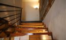 Eine Treppe aus Holz mit einer modernen Geländer. An der Wand ist ein Steinmuster zu sehen, und im Hintergrund leuchtet eine Wandlampe.