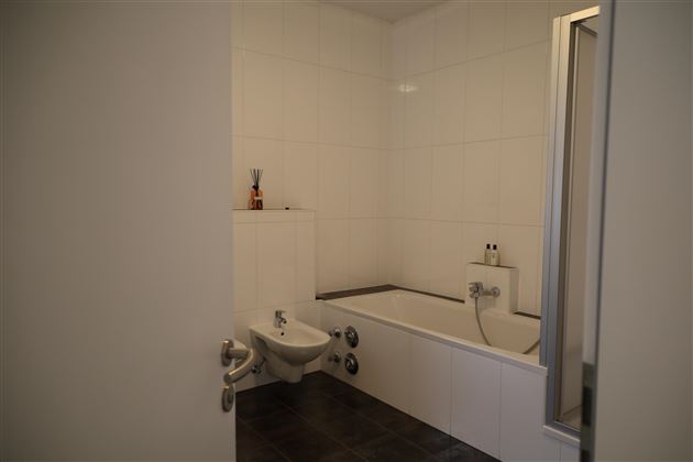 Ein modernes Badezimmer mit einer Badewanne und einer Dusche. Die Wände sind hell gefliest und der Boden ist dunkel.