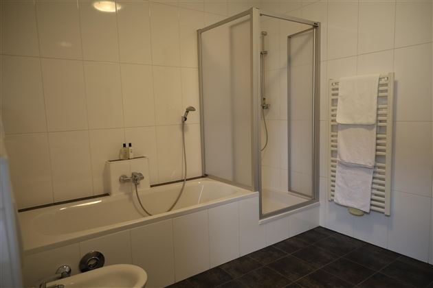 Ein modernes Badezimmer mit einer Badewanne und einer Duschkabine. Handtücher hängen an einem Handtuchheizkörper.