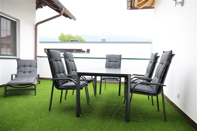 Ein modern gestalteter Balkon mit einem Tisch und sechs Stühlen. Der Boden ist mit grünem Rasen versehen und es herrscht eine ruhige Atmosphäre.