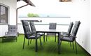 Ein modern gestalteter Balkon mit einem Tisch und sechs Stühlen. Der Boden ist mit grünem Rasen versehen und es herrscht eine ruhige Atmosphäre.