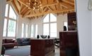 Ein modernes Wohnzimmer mit hohen Fenstern und Holzdecken. Es gibt eine offene Küche mit roten Möbeln und komfortablen Sitzmöglichkeiten.