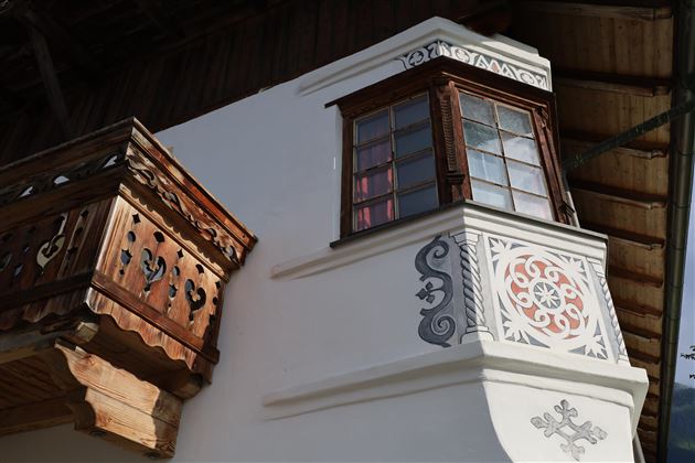 Eine detailreiche Fassade eines traditionellen Hauses mit einem Fenster und einem schönen Balkongeländer. Die Fassadenmalerei zeigt kunstvolle Designs.