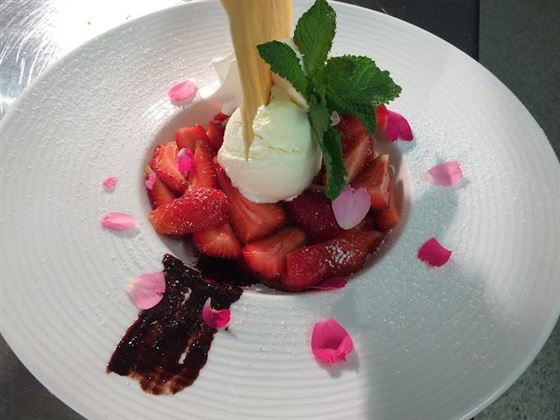 An artistic dessert with fresh strawberries, a scoop of vanilla ice cream, and a decorative sauce. The dish is garnished with edible flower petals and powdered sugar.