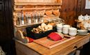 A rustic wooden counter with spice containers, a bread basket, and dishes. On the work surface lies a cutting board and a red cloth.