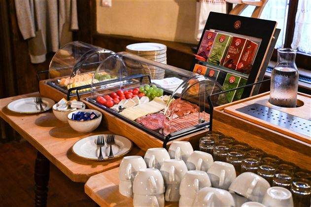 A lovingly arranged breakfast buffet with fresh fruits, sausage and cheese varieties. Dishes and glasses are neatly arranged on a table.