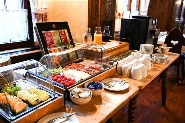 A rich breakfast buffet with fresh fruits, cold cuts, and drinks. The table is beautifully set and offers a cozy atmosphere.