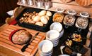 A richly set table with various types of bread and fresh rolls. There are also bowls with muesli, dried fruits, and nuts ready.