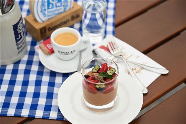 A delicious dessert in a glass with fresh berries and nuts. Next to it stands an espresso and a glass of water on a checkered table.