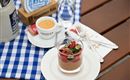 A delicious dessert in a glass with fresh berries and nuts. Next to it stands an espresso and a glass of water on a checkered table.