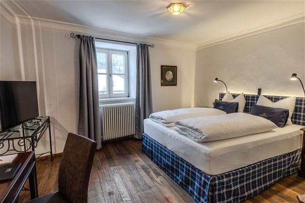 An elegant bedroom with a large double bed and cozy pillows. A desk and a television are also available, as well as a window with curtains.