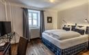 An elegant bedroom with a large double bed and cozy pillows. A desk and a television are also available, as well as a window with curtains.