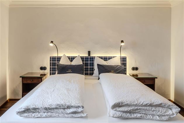 A cozy bedroom with two single beds and modern bedside lamps. The walls are painted in neutral colors, creating an inviting atmosphere.