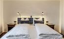 A cozy bedroom with two single beds and modern bedside lamps. The walls are painted in neutral colors, creating an inviting atmosphere.