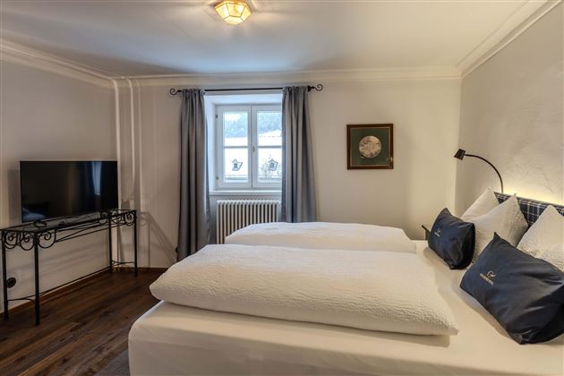 A modern bedroom with two single beds and a bright window front. A television and stylish wall decor complement the space.