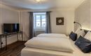 A modern bedroom with two single beds and a bright window front. A television and stylish wall decor complement the space.