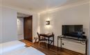 A modern room with a bed, a desk, and a television. The walls are light and the floor is made of wood.