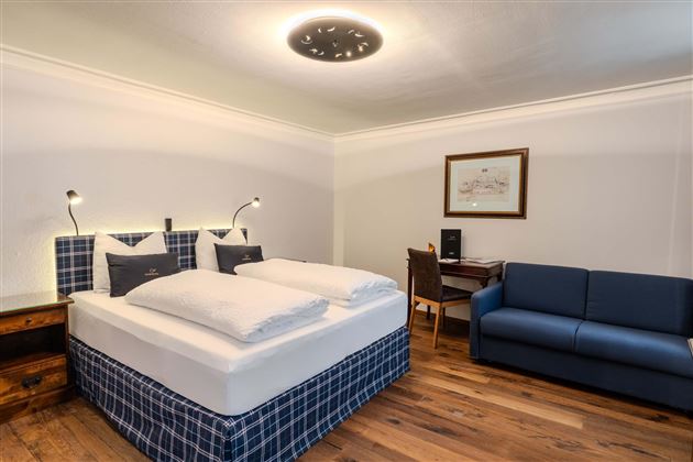 A modern bedroom with a comfortable double bed and a seating area. The room has a bright, inviting design and hardwood flooring.
