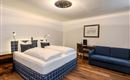 A modern bedroom with a comfortable double bed and a seating area. The room has a bright, inviting design and hardwood flooring.