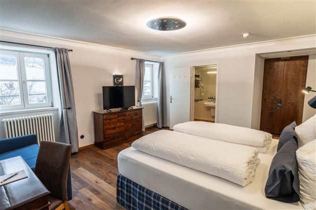 A modern hotel room with two beds and a table. Large windows provide plenty of daylight.