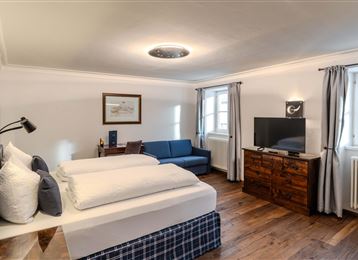 Una camera da letto moderna con due letti singoli e un comodo divano.
La stanza è luminosa e accogliente con pavimento in legno e grandi finestre.