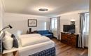 A modern bedroom with two single beds and a cozy sofa. The room is bright and friendly with wooden flooring and large windows.