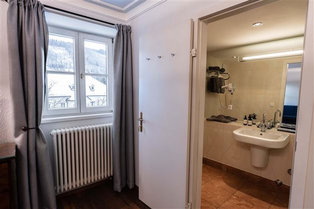 A bright room with a window and a radiator.  
On the right side is the bathroom with modern facilities.