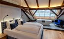 A modern bedroom with a double bed and exposed wooden beams. The large window front provides plenty of natural light and offers a comfortable atmosphere.