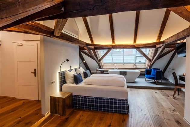 A modern room with two beds and slanted ceiling beams. Large windows provide plenty of light and a pleasant atmosphere.