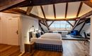 A modern room with two beds and slanted ceiling beams. Large windows provide plenty of light and a pleasant atmosphere.