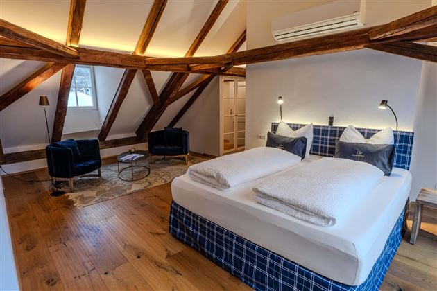 A modern bedroom with a large bed and wooden ceilings. There are two armchairs and a small table in the room.