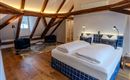 A modern bedroom with a large bed and wooden ceilings. There are two armchairs and a small table in the room.