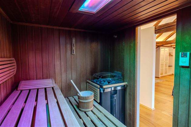 A modern sauna with wooden benches and colorful lights. In the background, there is a bucket and a stove.