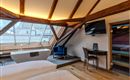 A cozy room with a wooden ceiling and modern furniture. There is a large window, a bathtub, and a television.