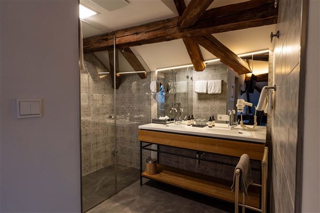 A modern bathroom with wooden details and a large shower. The washing area has an elegant wooden shelf and bright tiles.