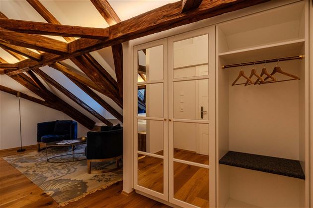 A cozy room in the attic with visible wooden beams. There is a wardrobe, a couch, and a stylish carpet.